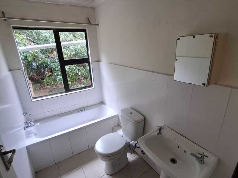 A functional bathroom featuring a bathtub, pedestal basin, and toilet with tiled walls and flooring, ready for modernization.