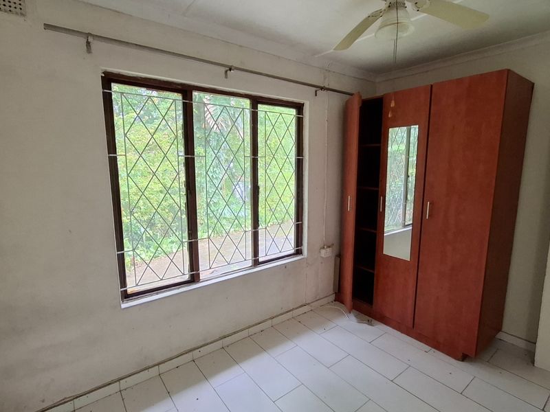 A bedroom featuring tiled flooring, a ceiling fan, and security bars on the window, requiring cosmetic updates to improve its overall condition.