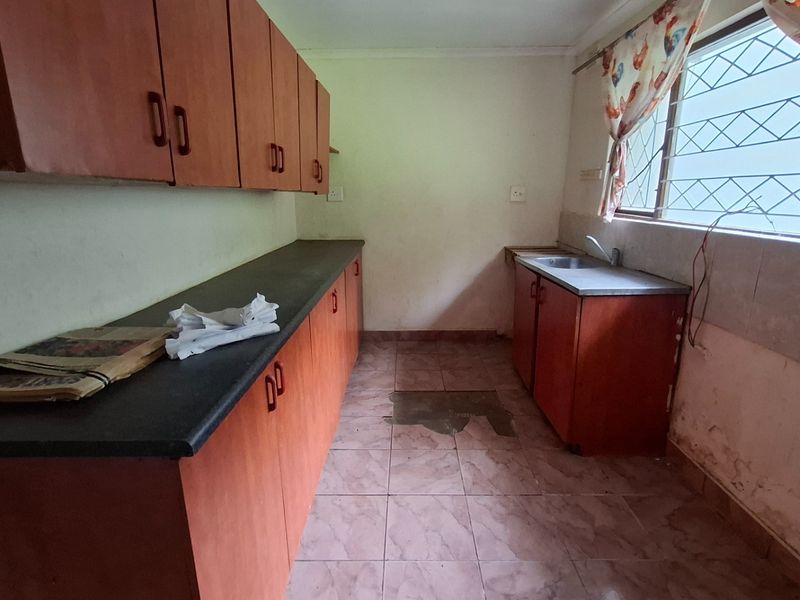 A dated kitchen featuring laminate cabinetry, tiled flooring, and a stainless steel sink, requiring renovation and repairs to address wall and floor damage.