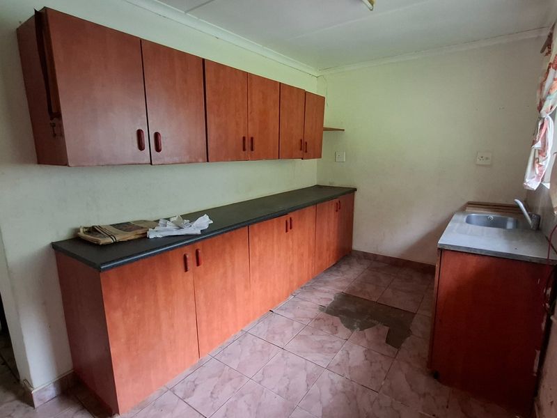 A dated kitchen featuring laminate cabinetry, dark countertops, and a stainless steel sink, requiring cosmetic updates to improve functionality and aesthetic appeal.