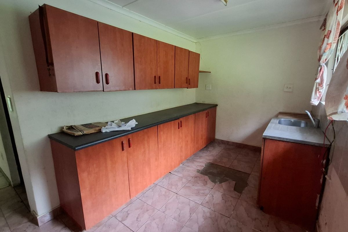 A dated kitchen featuring laminate cabinetry, dark countertops, and a stainless steel sink, requiring cosmetic updates to improve functionality and aesthetic appeal.