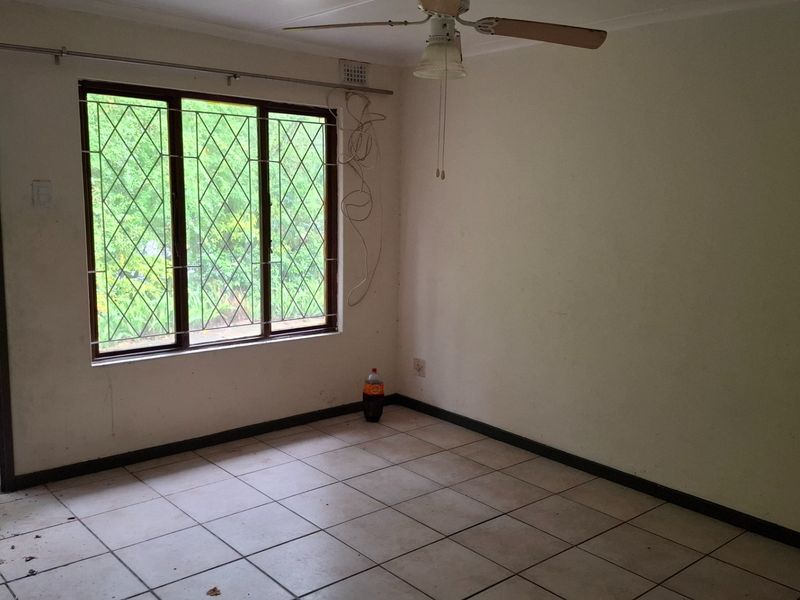 An empty living room featuring tiled flooring, a ceiling fan, and a sliding door providing access to the exterior garden area.
