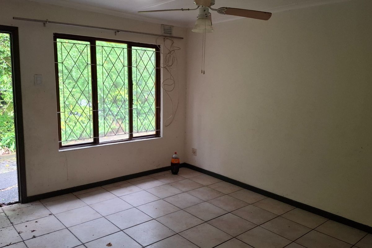 An empty living room featuring tiled flooring, a ceiling fan, and a sliding door providing access to the exterior garden area.