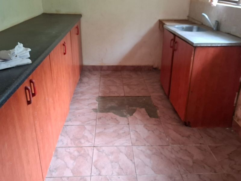 A dated kitchen area featuring laminate cabinetry, a stainless steel sink, and damaged flooring requiring repair and renovation.