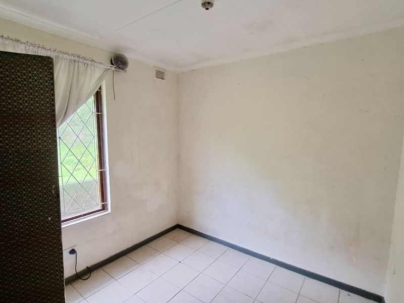 An empty bedroom featuring tiled flooring, a window with security bars, and a built-in security gate, requiring cosmetic updates to the walls and ceiling.