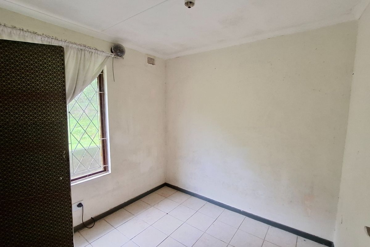 An empty bedroom featuring tiled flooring, a window with security bars, and a built-in security gate, requiring cosmetic updates to the walls and ceiling.