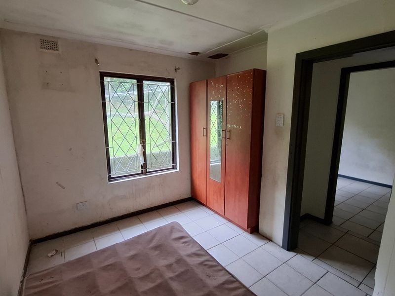 A bedroom featuring tiled flooring and a window with a security gate, currently requiring cosmetic updates and wall repairs.