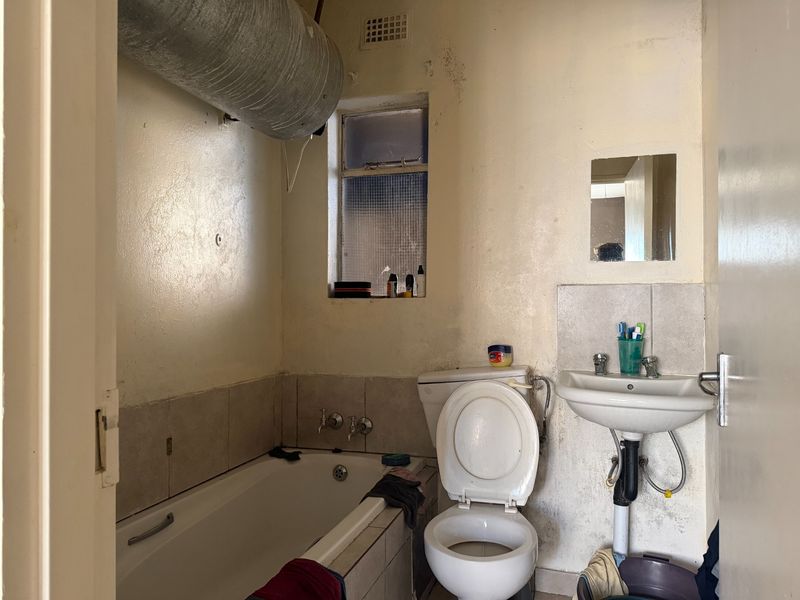 A dated bathroom featuring a bathtub, pedestal basin, and toilet, requiring significant renovation and cosmetic repairs to address wall damage and exposed infrastructure.