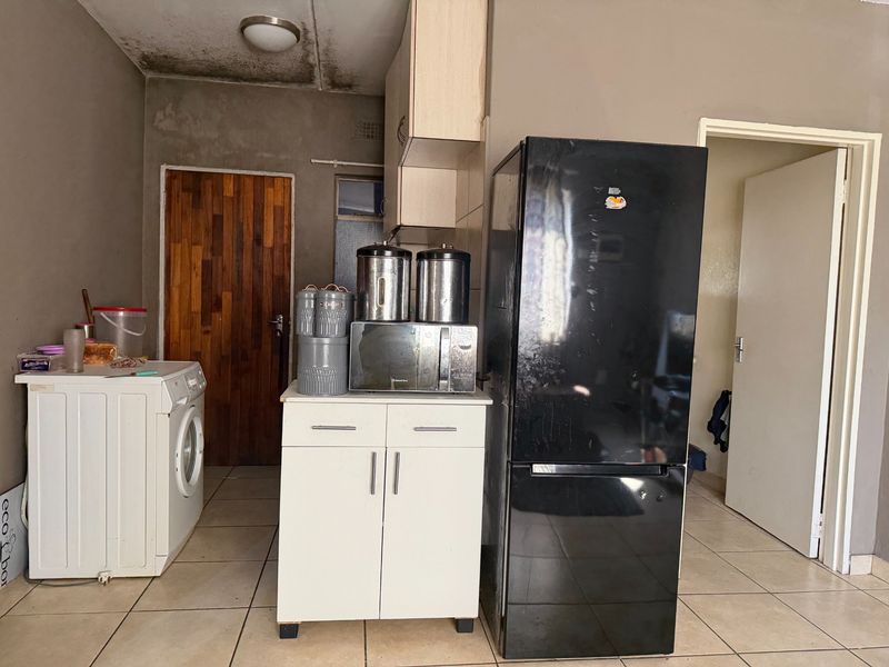 A functional kitchen area featuring tiled floors, built-in cabinetry, and a timber door, currently requiring maintenance and cosmetic updates to the ceiling and walls.