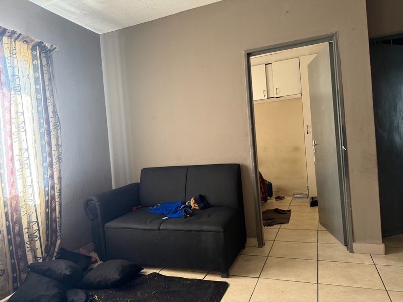 A living area featuring tiled flooring and a doorway leading to an adjacent room with built-in storage cupboards.