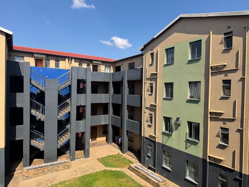 Exterior view of an apartment complex featuring a central courtyard, external staircases, and multi-story residential blocks with security bars on windows.