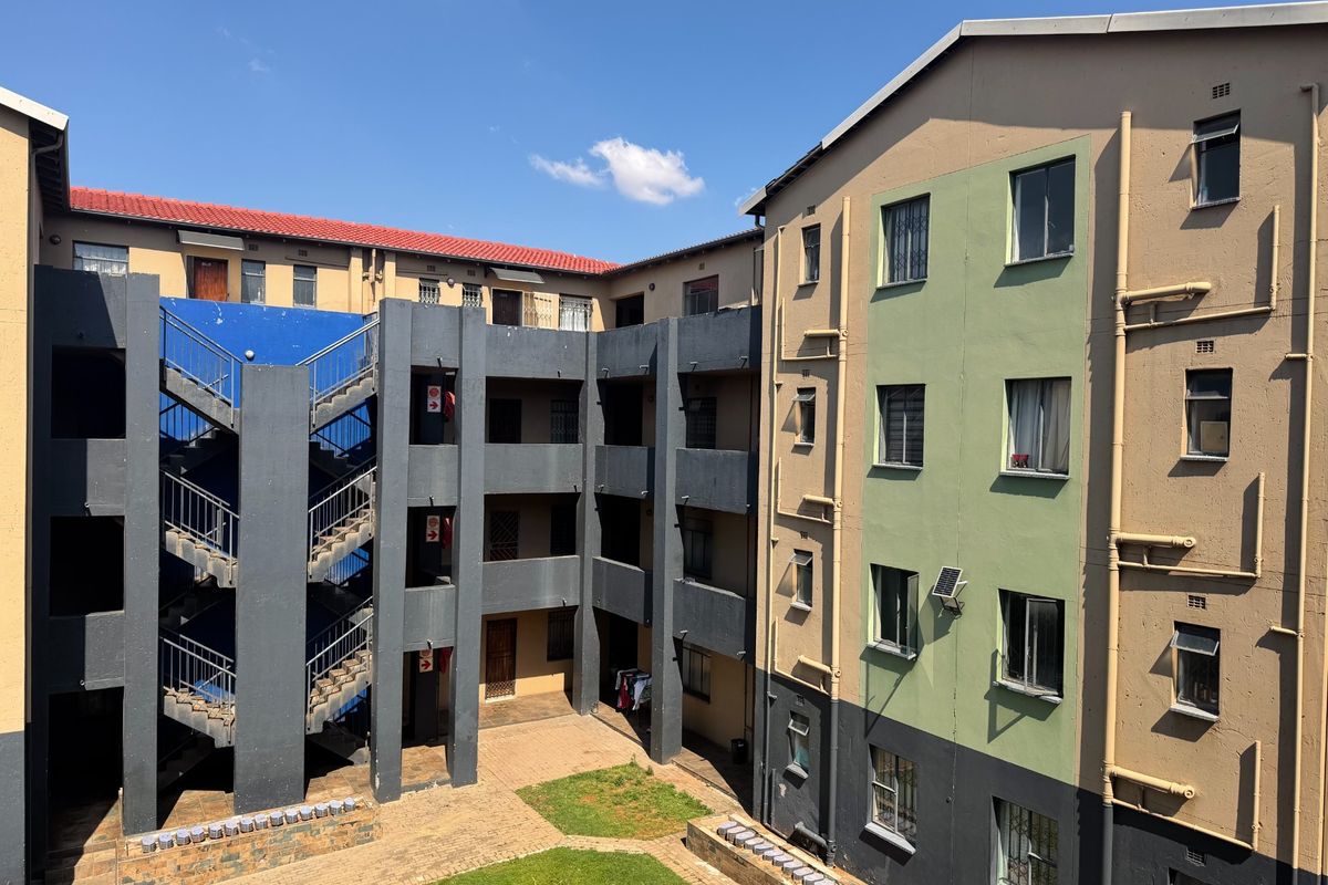 Exterior view of an apartment complex featuring a central courtyard, external staircases, and multi-story residential blocks with security bars on windows.