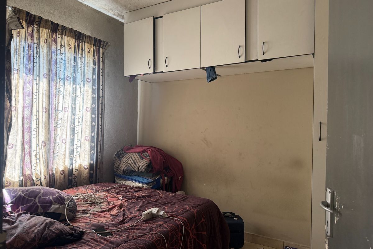 A compact bedroom featuring built-in overhead storage cupboards and tiled flooring, currently requiring cosmetic updates to the walls and ceiling.