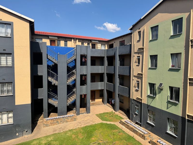 Exterior view of an apartment complex courtyard featuring a central staircase, paved walkways, and communal garden area.