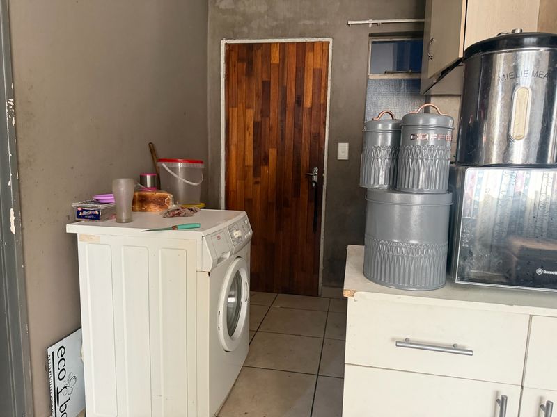 A functional laundry area featuring tiled flooring, built-in cabinetry, and a dedicated washing machine space, requiring cosmetic updates to the walls and finishes.