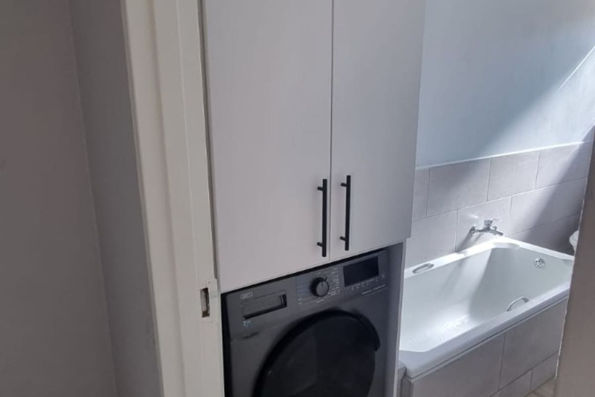 Bathroom featuring a built-in laundry cupboard with integrated washing machine, bathtub, and neutral tiled finishes.