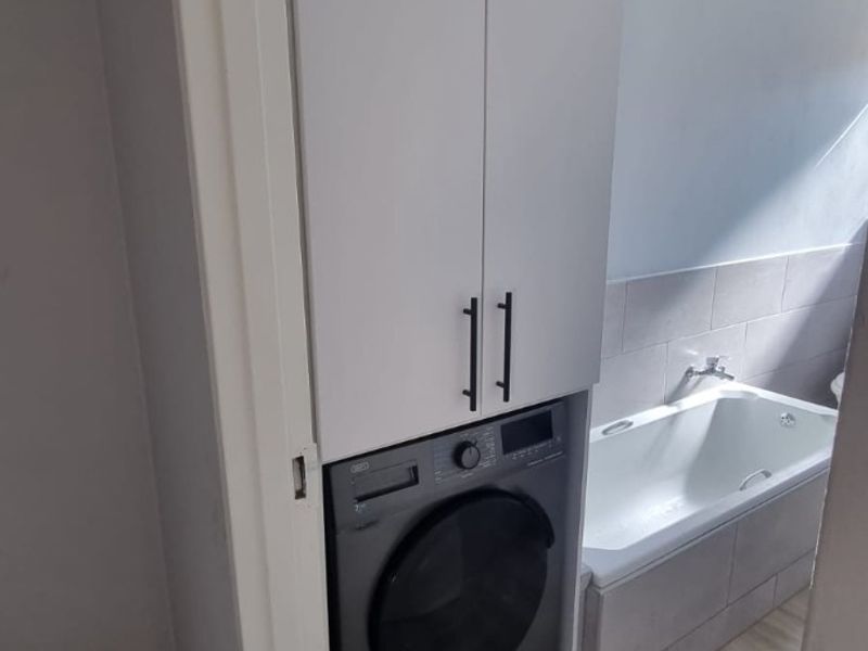 Bathroom featuring a built-in laundry cupboard with integrated washing machine, bathtub, and neutral tiled finishes.