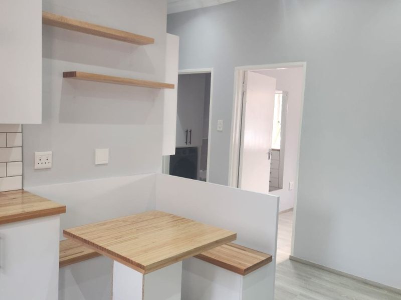 Modern kitchen area featuring a built-in breakfast nook with timber seating and table, floating shelves, and light-toned laminate flooring.