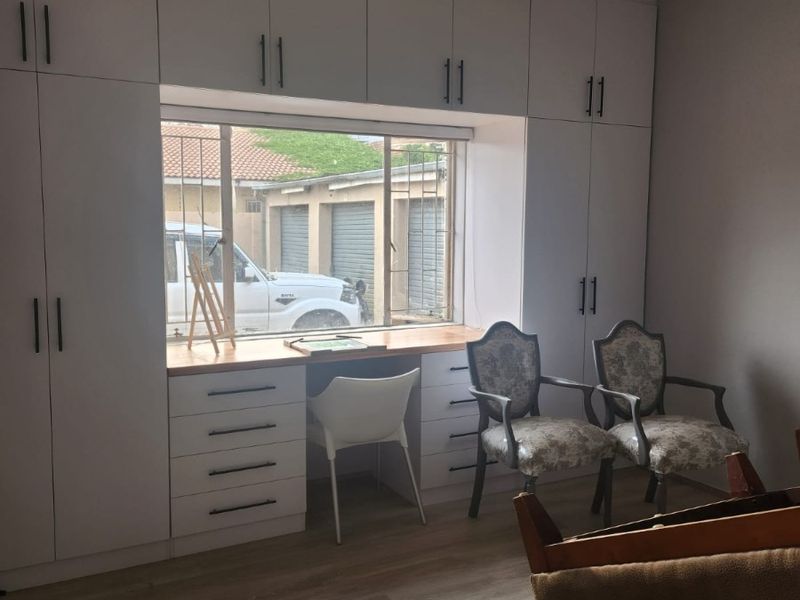 A bedroom featuring extensive white built-in cabinetry with an integrated desk workspace, laminate flooring, and recessed lighting.