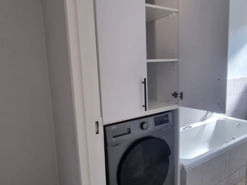 Bathroom featuring a built-in laundry cupboard with integrated washing machine space and a tiled bathtub, currently requiring minor finishing work to skirting and walls.