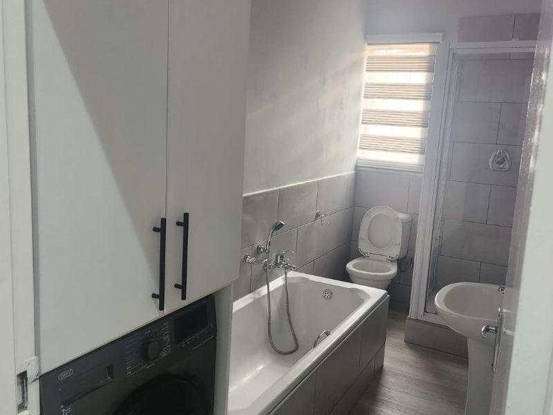 A functional bathroom featuring a bathtub, separate shower enclosure, pedestal basin, toilet, and integrated laundry cabinetry with a built-in washing machine.