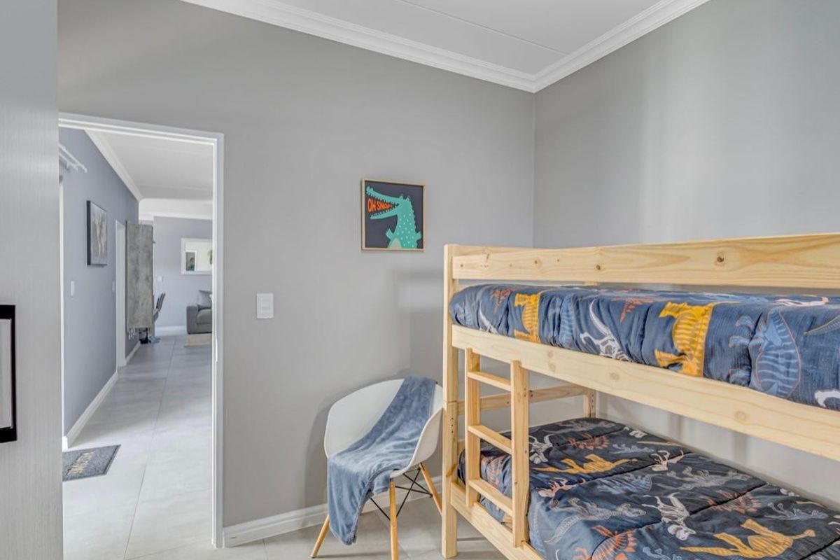 A well-maintained bedroom featuring neutral grey walls, crown molding, and light-colored floor tiles, with a clear view into the adjacent hallway.