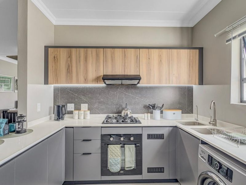 Modern U-shaped kitchen featuring sleek grey and wood-grain cabinetry, stone countertops, integrated gas hob, oven, extractor fan, and a stylish tiled backsplash.