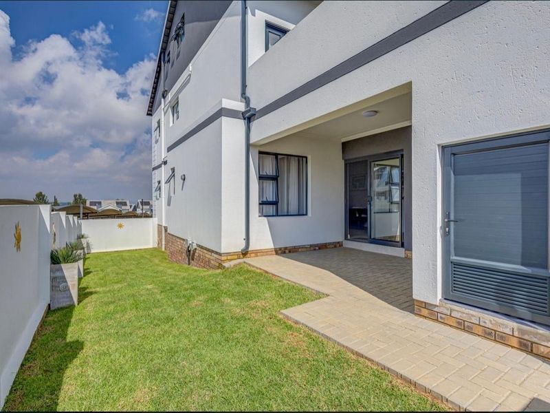 A well-maintained rear exterior view featuring a paved patio area, a small private lawn, and modern building finishes.