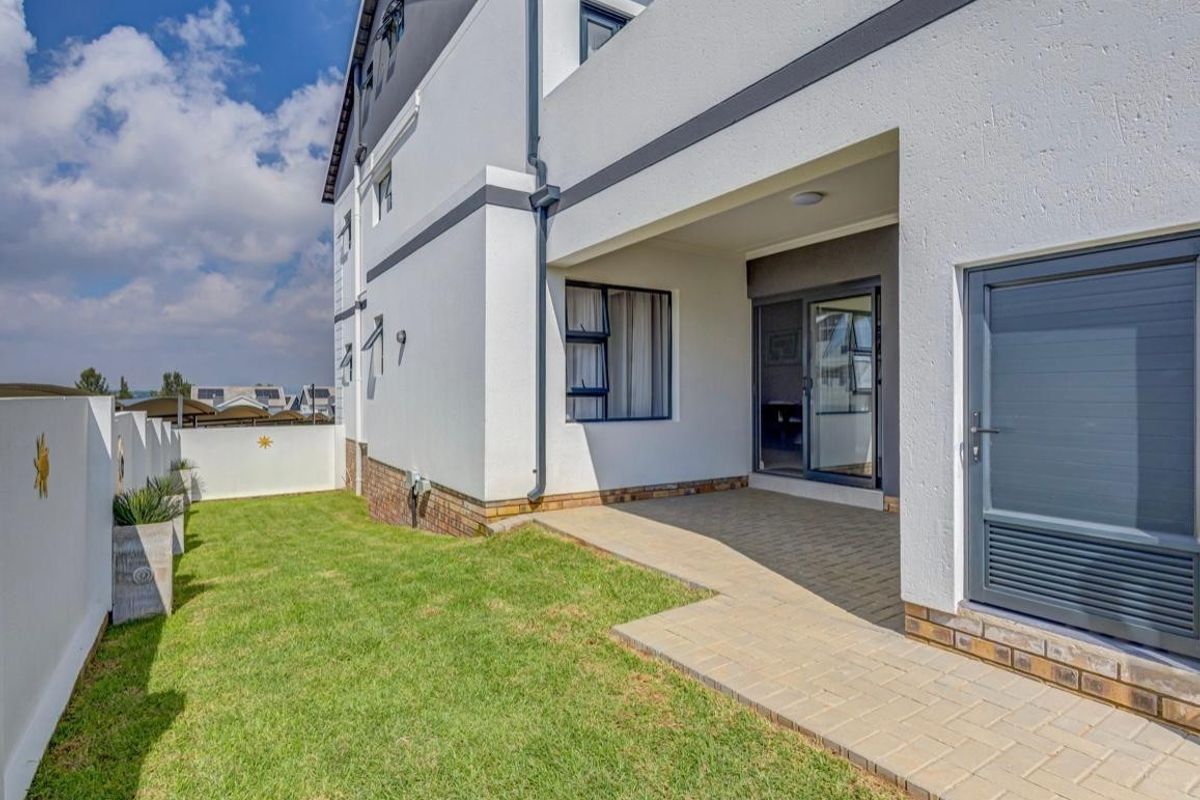A well-maintained rear exterior view featuring a paved patio area, a small private lawn, and modern building finishes.