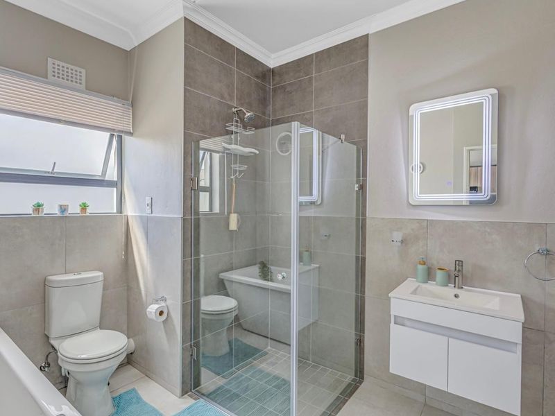 Modern bathroom featuring a glass shower enclosure, wall-mounted vanity with LED mirror, bathtub, and neutral tiled finishes.