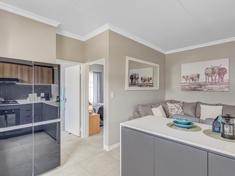 Modern open-plan kitchen and living area featuring sleek cabinetry, stone countertops, gas hob, and neutral tiled flooring, leading to an adjacent bedroom.