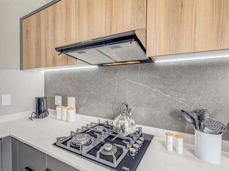 Modern kitchen featuring wood-grain cabinetry, a stone splashback, integrated under-cabinet lighting, and a built-in gas hob with an extractor fan.