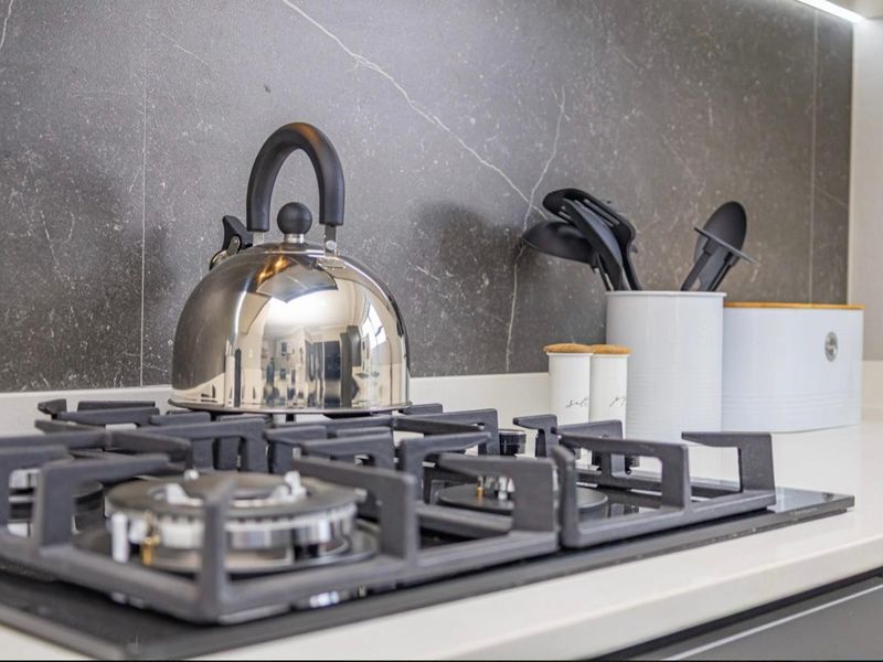 Modern kitchen featuring a sleek gas hob, stone splashback, and clean stone countertops, showcasing a contemporary and well-maintained cooking area.