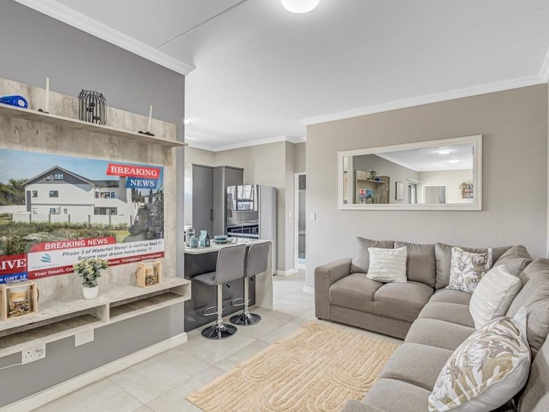 Modern open-plan living area featuring a kitchen island, built-in shelving, and neutral tiled flooring, creating a seamless flow between the kitchen and lounge space.