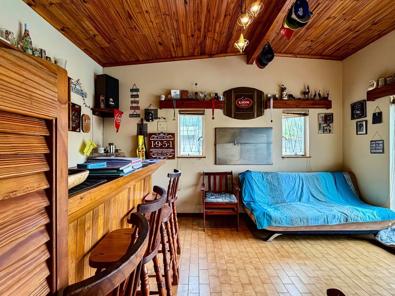 A rustic bar area featuring a built-in wooden counter, timber ceiling, and tiled flooring, with direct access to an outdoor space via sliding doors.