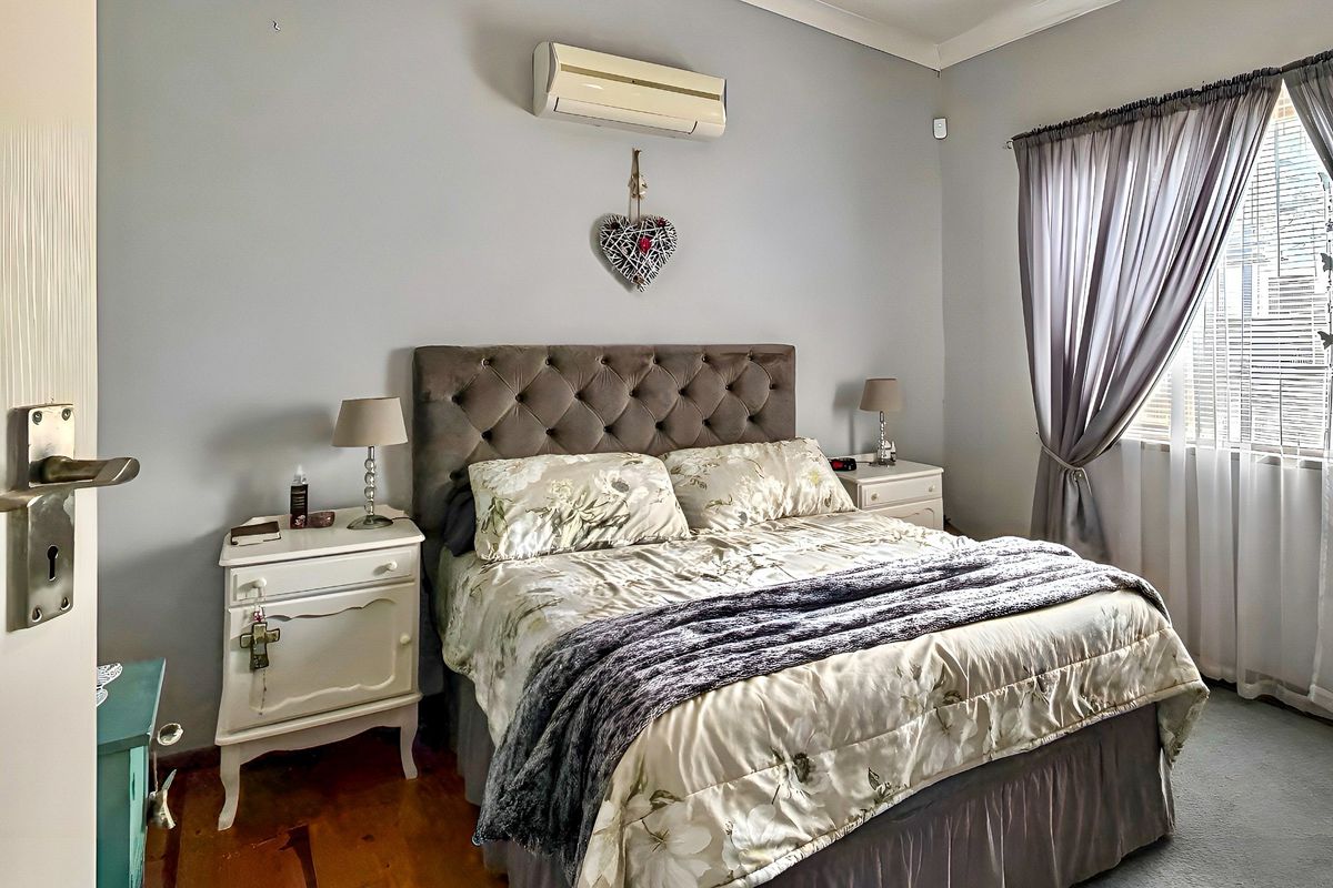 A bedroom featuring timber flooring and a wall-mounted air conditioning unit, providing a functional space with neutral wall finishes.