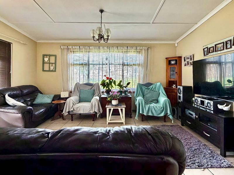 A comfortable living room featuring tiled flooring, a central chandelier, and large windows with blinds, offering a functional and well-lit space.