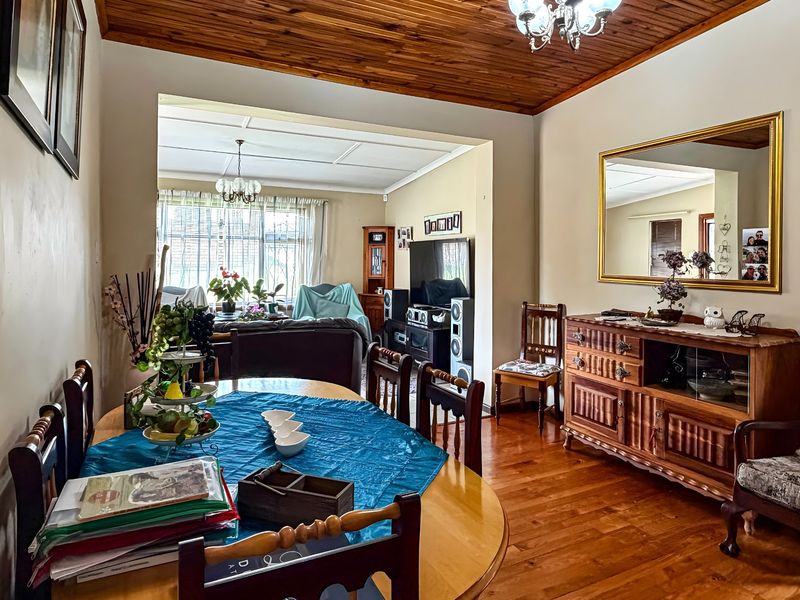 Open plan dining and living area featuring warm hardwood flooring and a traditional timber-paneled ceiling.