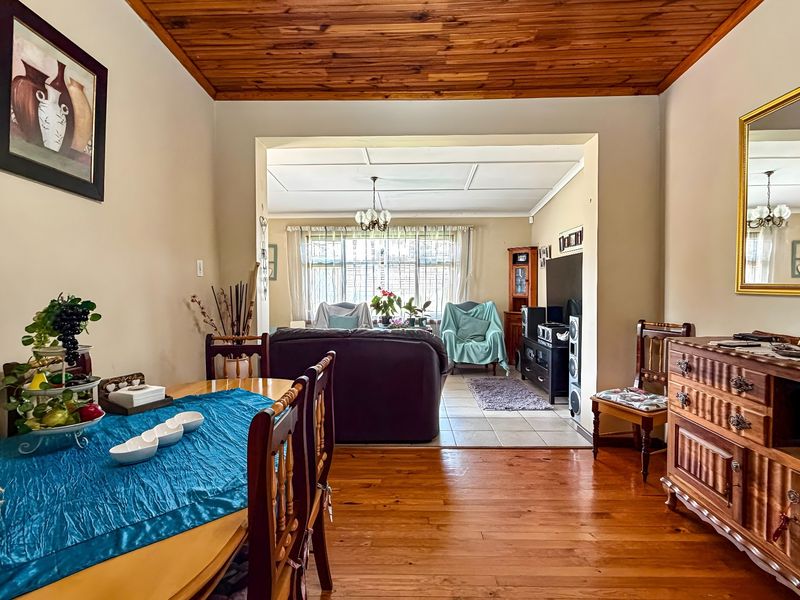 Open plan living and dining area featuring hardwood flooring, a timber-paneled ceiling, and a seamless transition to a tiled lounge space with large windows.