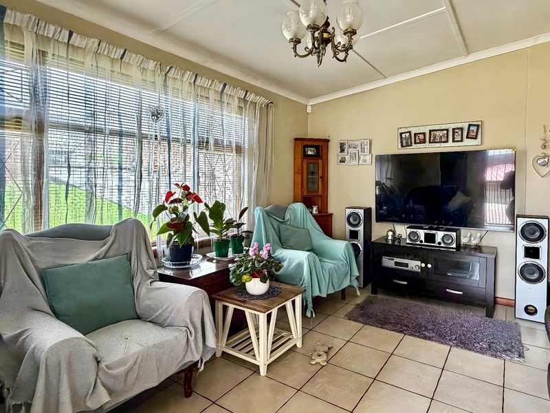 A comfortable living room featuring tiled flooring, a large window with security bars, and a central ceiling light fixture.
