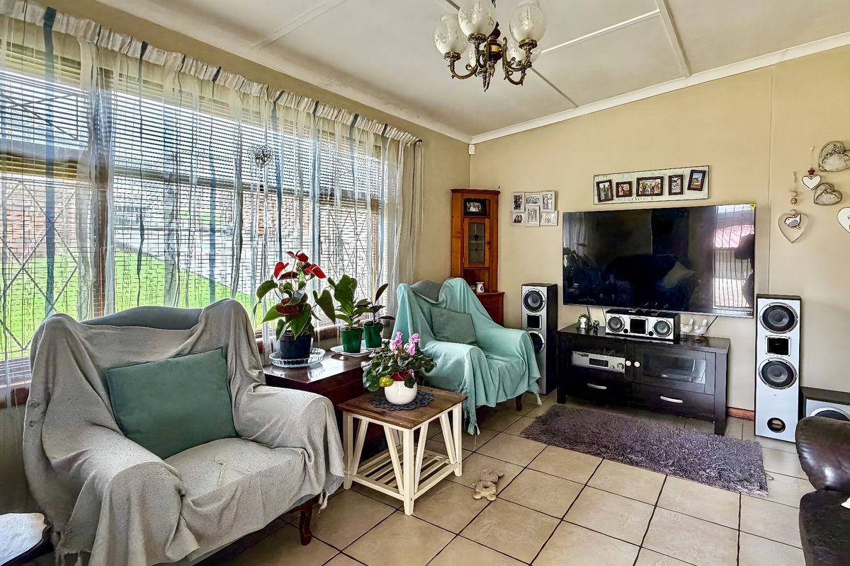 A comfortable living room featuring tiled flooring, a large window with security bars, and a central ceiling light fixture.