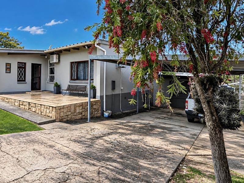 Front view of the property featuring a paved driveway, attached carport, and a raised patio area with stone cladding detail.