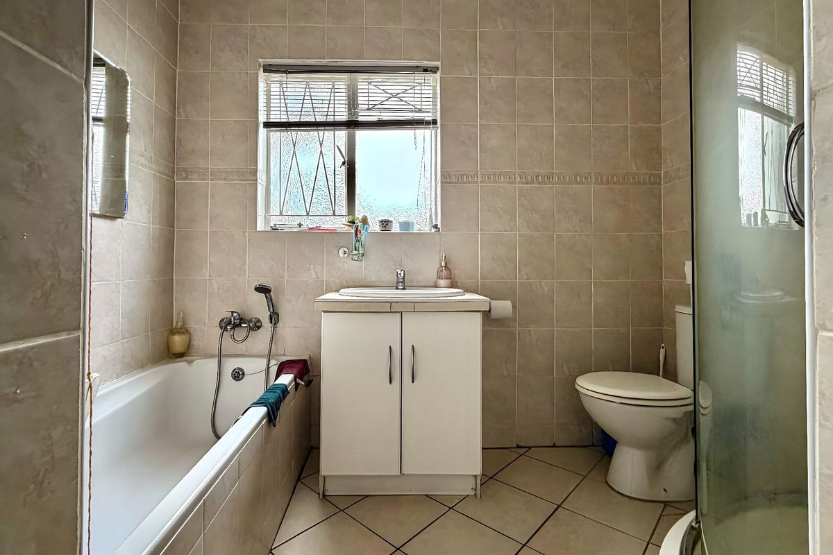 A functional bathroom featuring a bathtub, vanity basin, toilet, and separate shower enclosure with neutral wall and floor tiling.