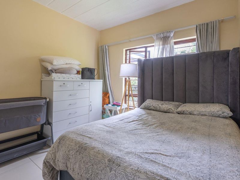 A functional bedroom featuring tiled flooring and a window fitted with security bars, providing natural light and ventilation.