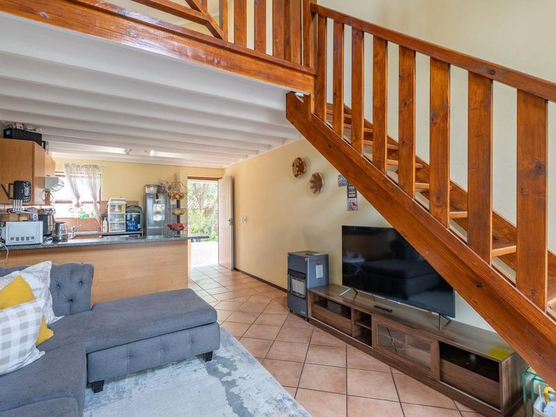 Open-plan living area featuring a wooden staircase, exposed ceiling beams, and a functional kitchen with tiled flooring throughout.