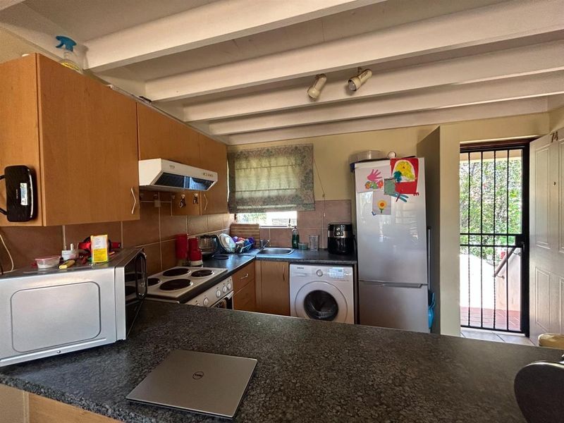 Compact kitchen featuring laminate cabinetry, granite countertops, an electric stove with extractor fan, and exposed ceiling beams, with direct access to an exterior security gate.
