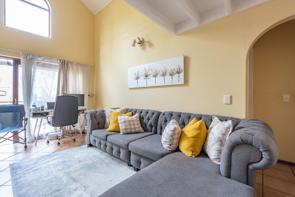 Spacious living room featuring high vaulted ceilings with exposed beams, tiled flooring, and an arched doorway leading to adjacent areas.
