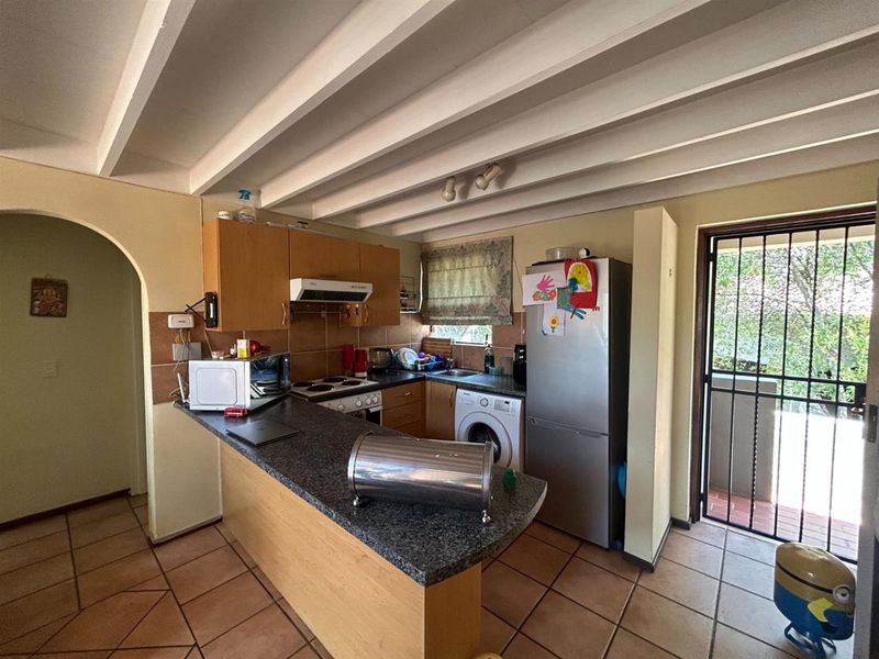 Functional kitchen featuring granite countertops, laminate cabinetry, exposed beam ceilings, and direct access to an outdoor area through a security gate.