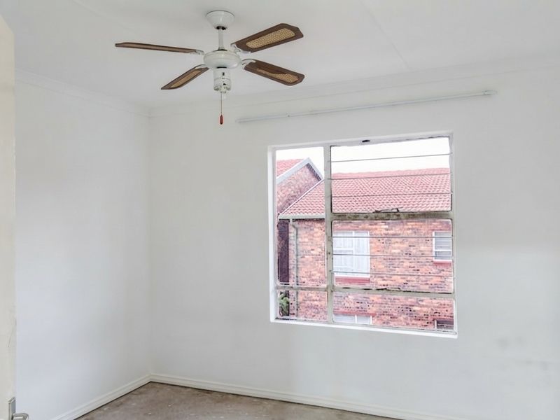 An empty bedroom featuring a ceiling fan and a louver window, offering a blank canvas for personalization.