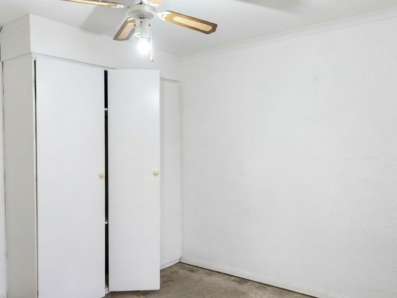 An empty bedroom featuring a built-in wardrobe and a ceiling fan, requiring cosmetic updates to the flooring and walls.